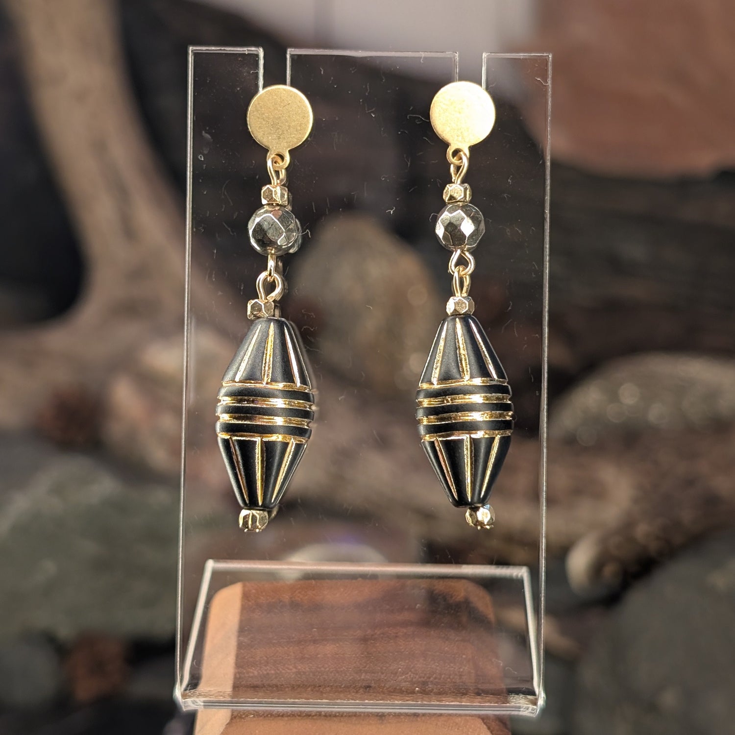Pair of gold and black earrings on a clear stand with a natural background