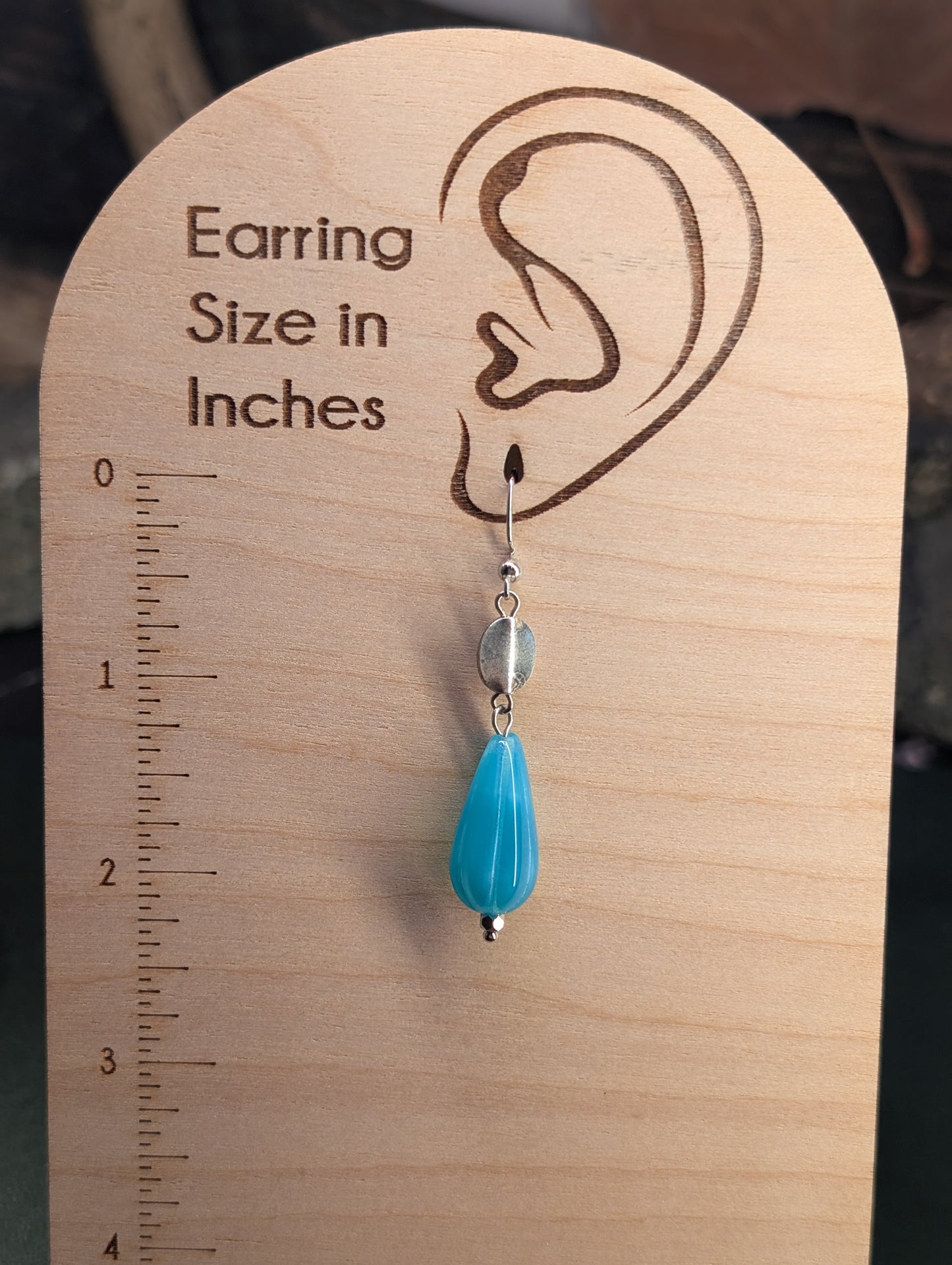 Earring on a wooden scale showing its size in inches